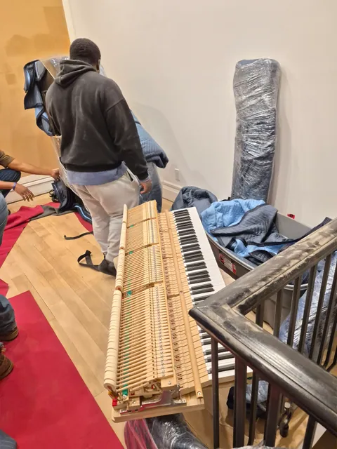 Detached piano keyboard and action assembly beside wrapped components and moving blankets
